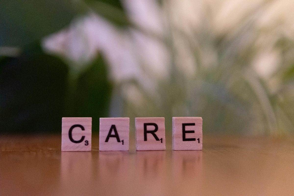Close-up of wooden tiles spelling 'CARE' on a table with a blurred background, evoking a sense of support.